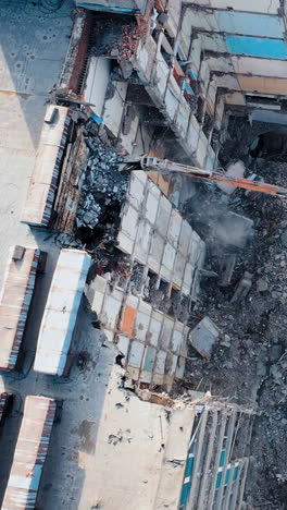 tractor with a special bucket dismantles a collapsed building after a disaster. construction work in the city. shooting from the air. vertical video