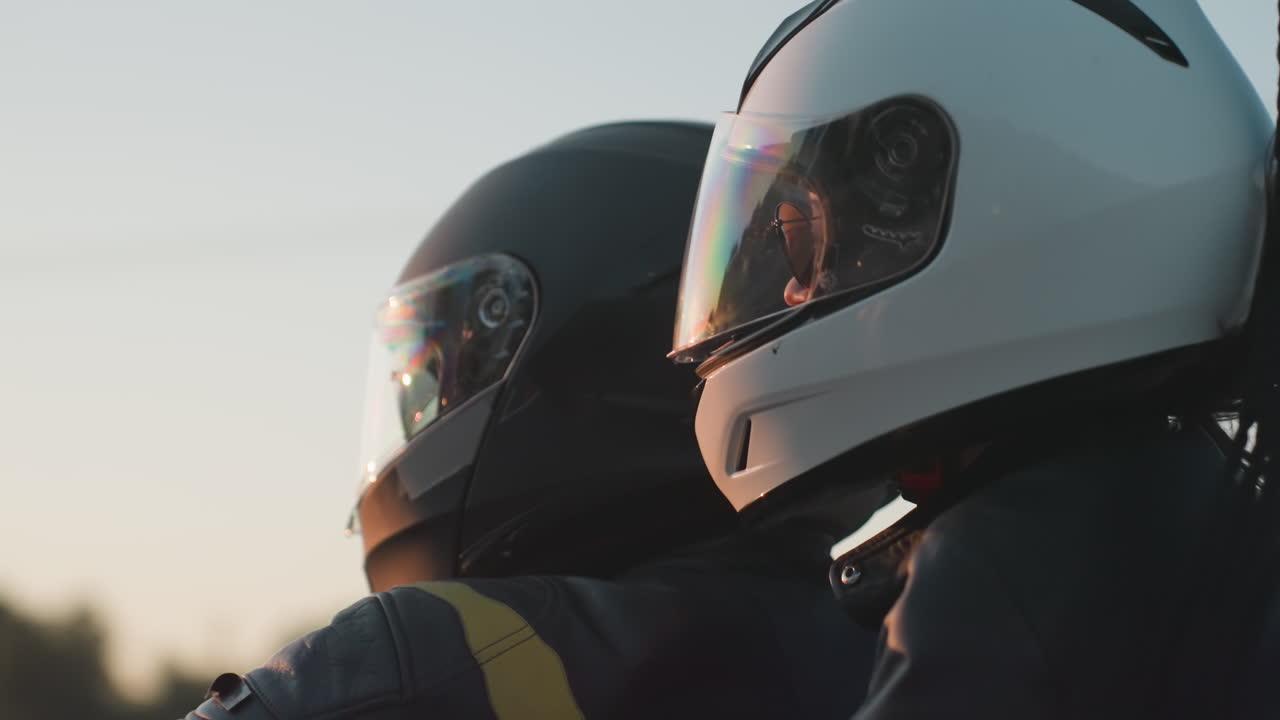 Close up of motorcycle rider with passenger wearing helmets traveling on road trip during sunset, warm light reflecting on visor, capturing freedom and adventure