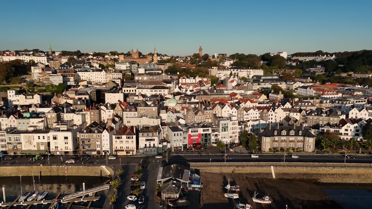 Riprese drone a St Peter Port, Guernsey, dal Crown Pier con l'Elizabeth College prominente nello skyline che mostra il lungomare e gli edifici della città che si ergono dietro in una giornata di sole con cielo azzurro senza nuvole