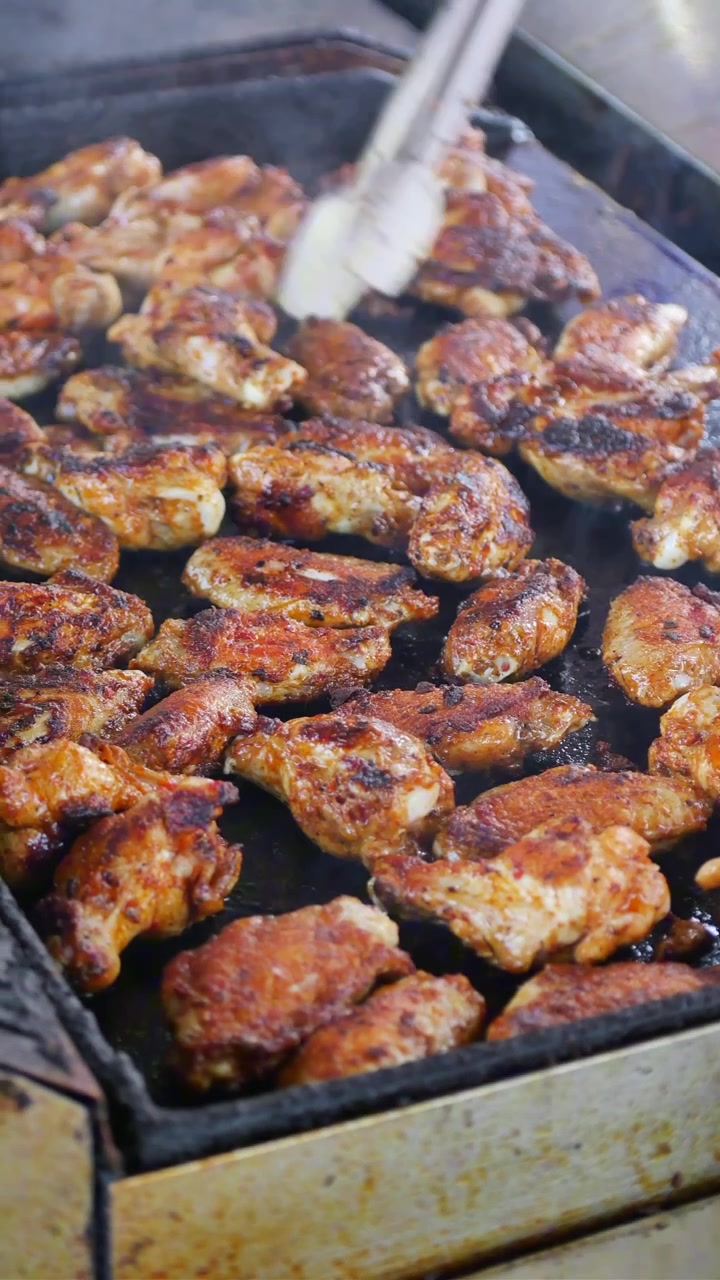 Ali di pollo dorate che grigliano su una piastra calda