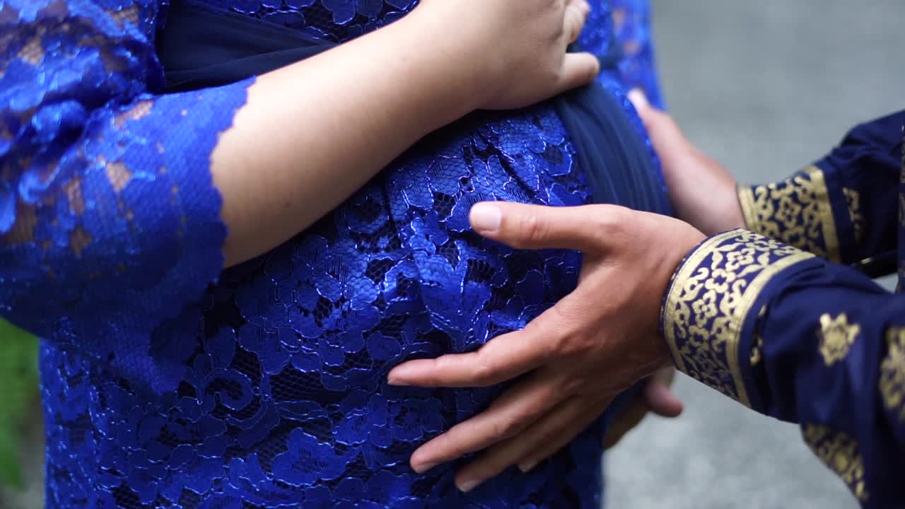 Couple at garden holding a pregnant woman's belly. Close up shot