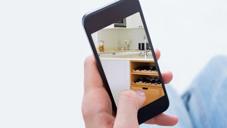 Person-holding-smartphone-with-modern-kitchen-interiors-displayed-on-screen