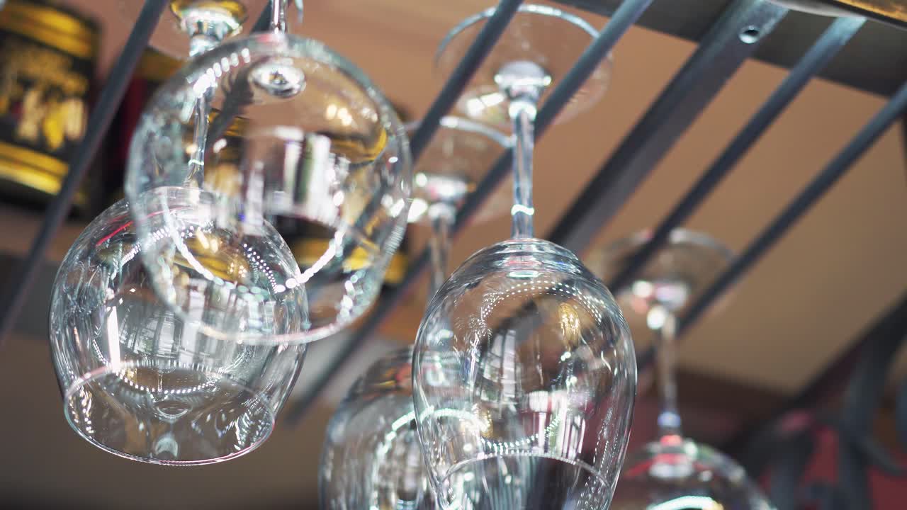 Clean empty wine glasses hanging on a rack and a hand adding washed glasses to a glassware holder in a bar.