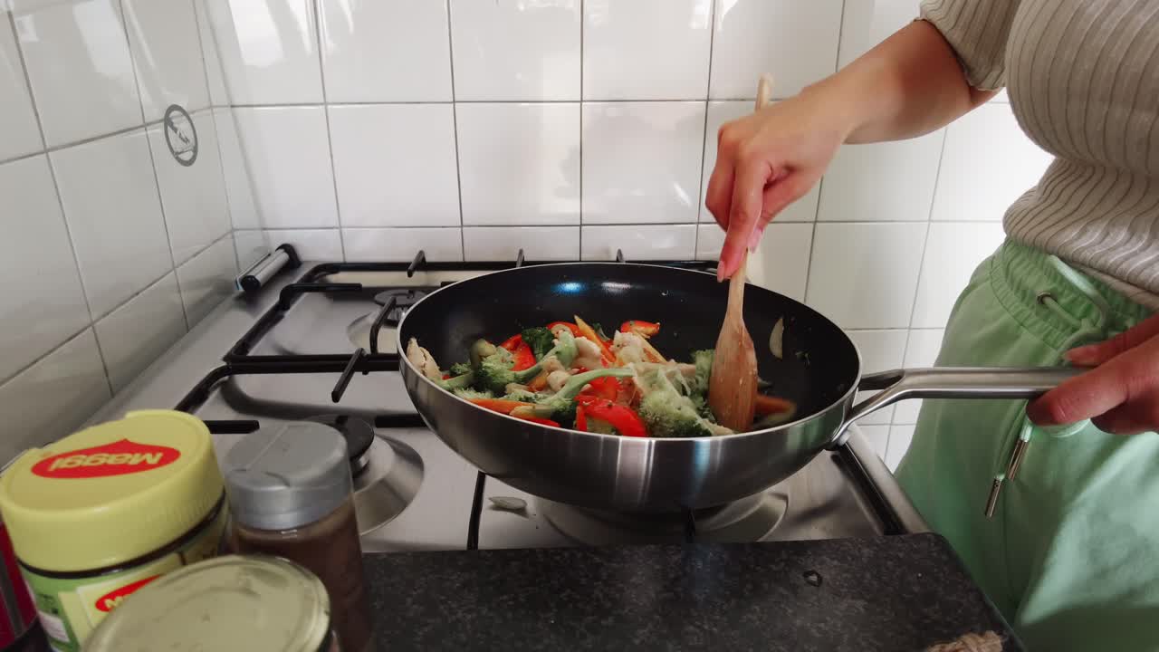mujer revuelve una cuchara de madera en una sartén llena de verduras, brócoli y pimientos
