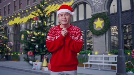 asian man in santa suit holding his hands in plea and making a cute face while standing in christmas night