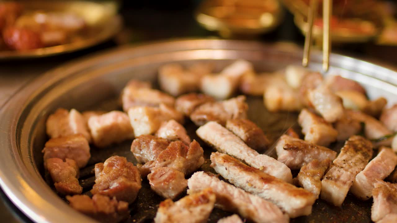 Chopsticks turn sizzling pork and vegetables on a hot grill, warm lighting, shallow focus