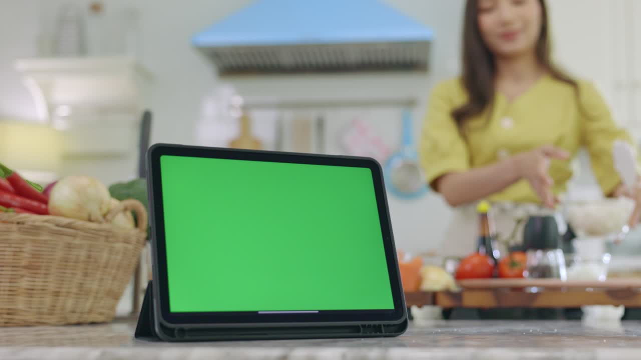 tableta con una pantalla verde con un hermoso fondo cocinando en la casa con una cara feliz, la esposa hace el desayuno felizmente en su casa.