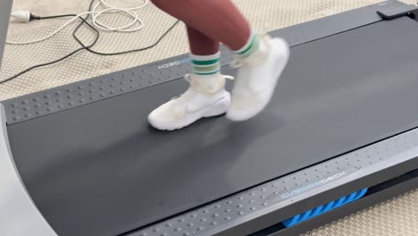 close-up of feet walking on a treadmill in a home gym, captured in slow motion with natural lighting
