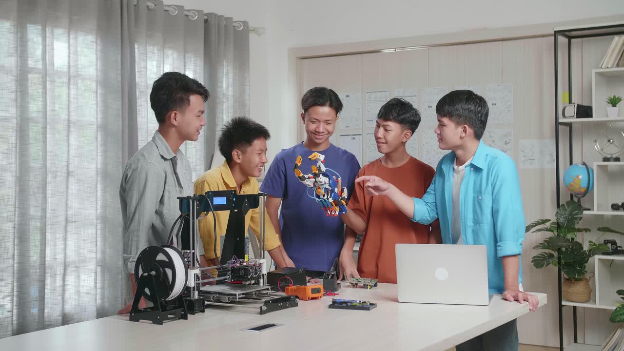 노트북과 3d 프린팅을 가진 젊은 아시아 소년 그룹이 사이보그 손을 확인하고 집에서 일하는 성공을 축하합니다.