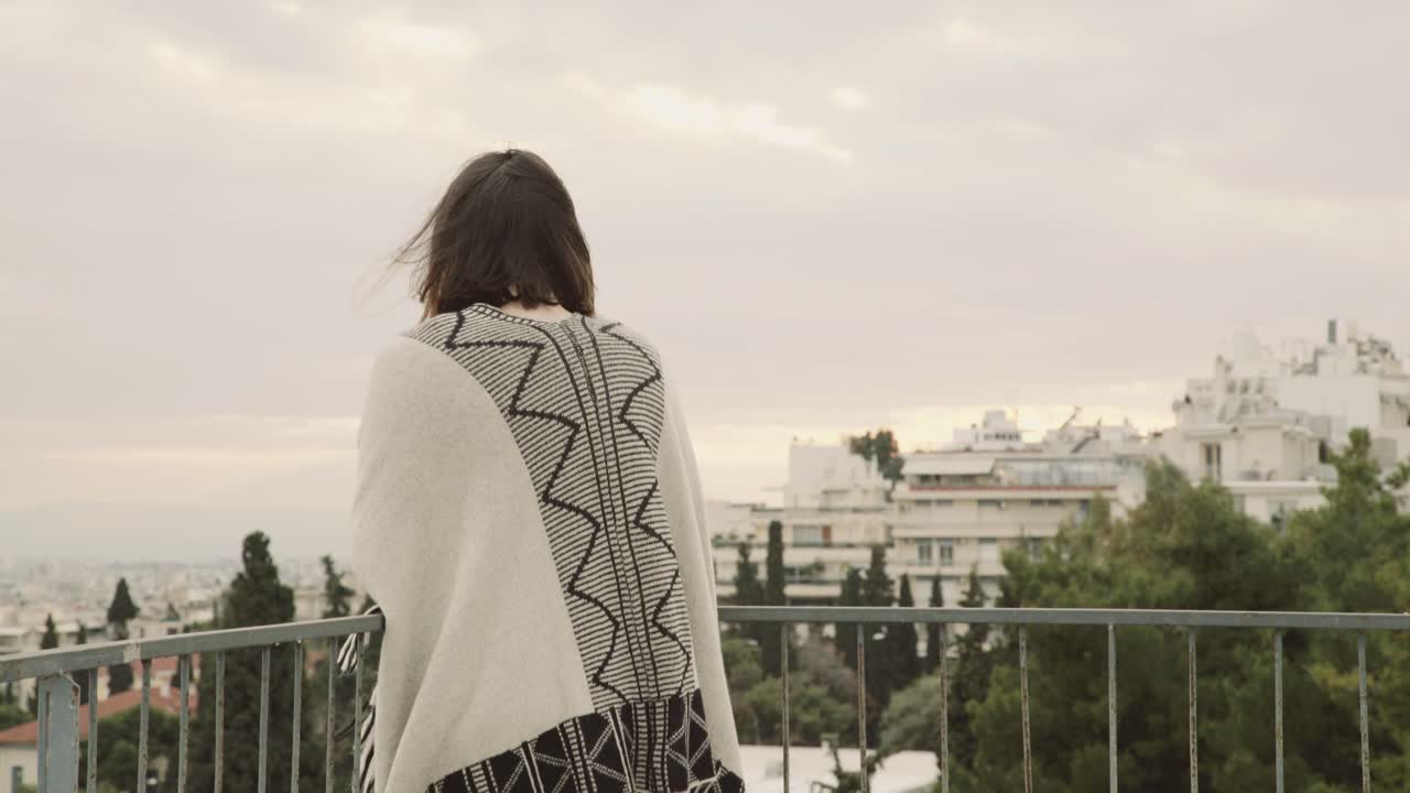 young woman standing on balcony and looking the city view wind moves her hair grey cloudy day