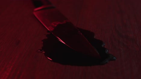 suspenseful dolly of a blood covered kitchen knife in a puddle of blood with flashing police lights in the background