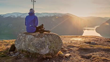 man sits on rock on mountain, sunset view over fjord