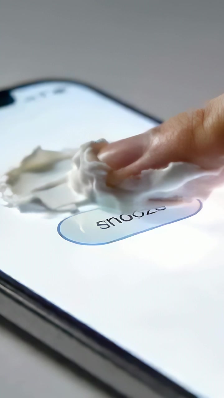 Vertical video: Pressing finger smearing cream across phone screen on desk, hiding snooze as alarm