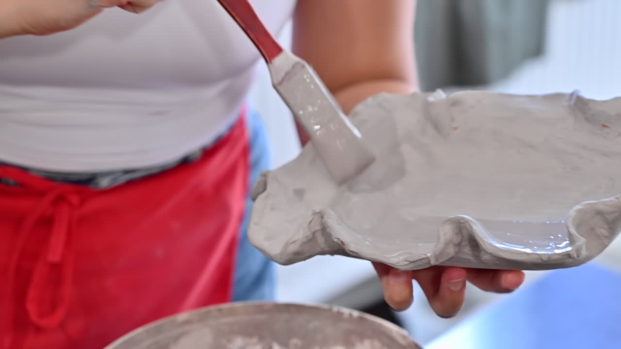Woman painting an orange plate made out of clay with white