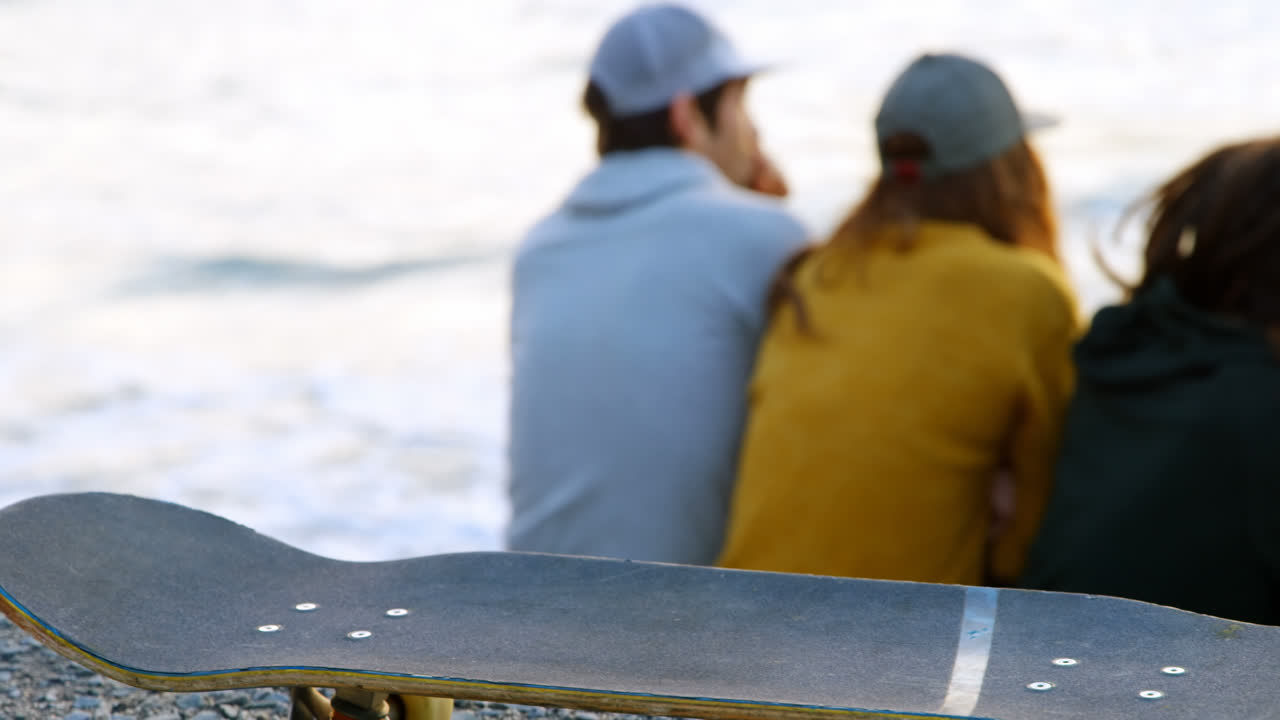 vista trasera de jóvenes amigos caucásicos sentados en una roca y mirando al mar en la playa 4k
