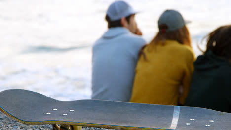 Rückansicht-Junger-Kaukasischer-Freunde,-Die-Auf-Einem-Felsen-Sitzen-Und-Am-Strand-Auf-Das-Meer-Schauen,-4k