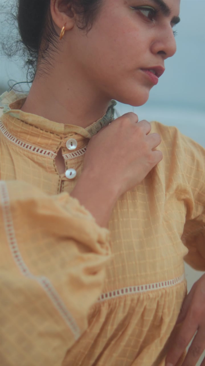 Donna in abito giallo che muove le braccia con grazia all'aperto, con illuminazione naturale soffusa.