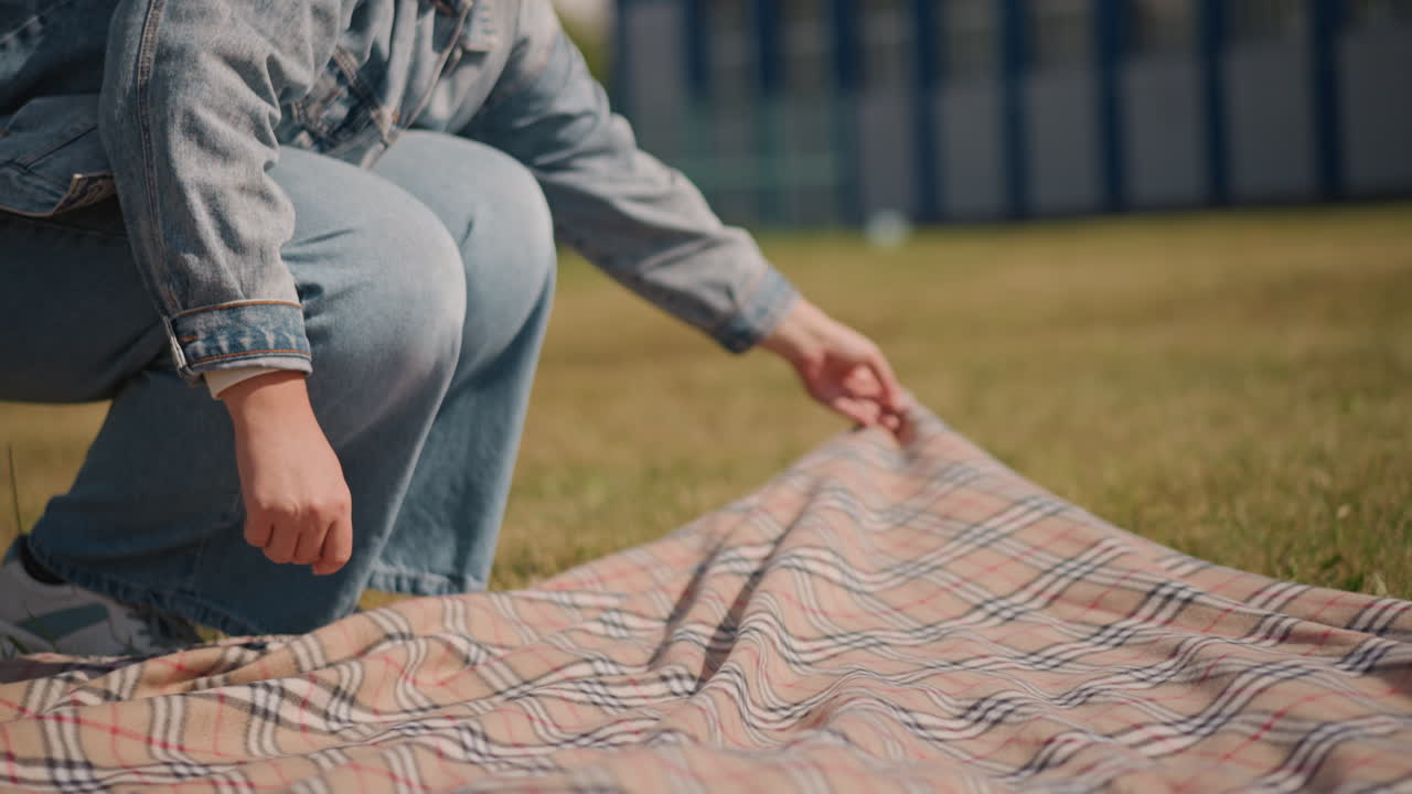 Sunlit scene with woman adjusting blanket. Woman carefully straightening plaid blanket on grassy lawn. Intimate moment of woman smoothing checkered blanket on bright sunlit grass field