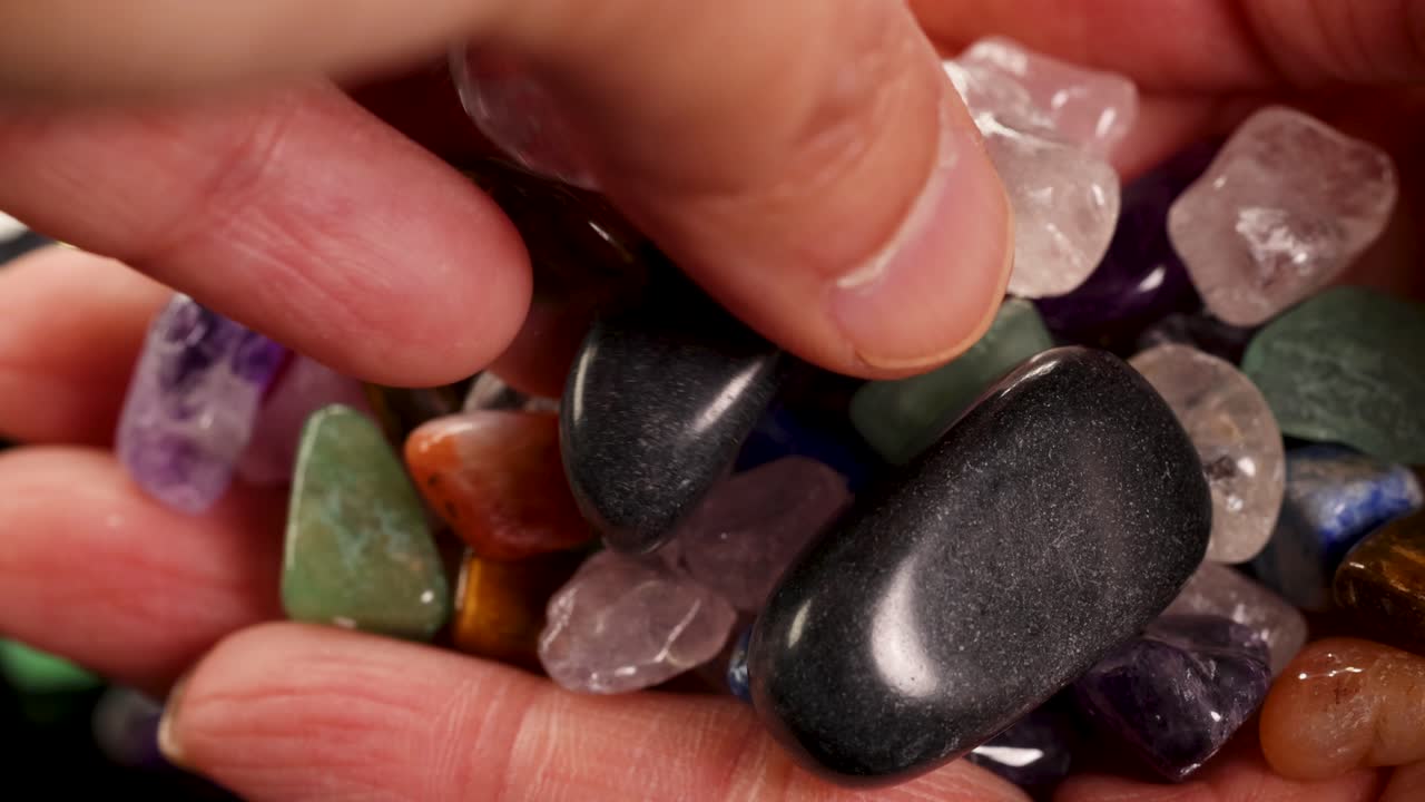 Uma visão em close-up de mãos segurando várias pedras de chakra coloridas, realçando texturas e cores sob iluminação suave.