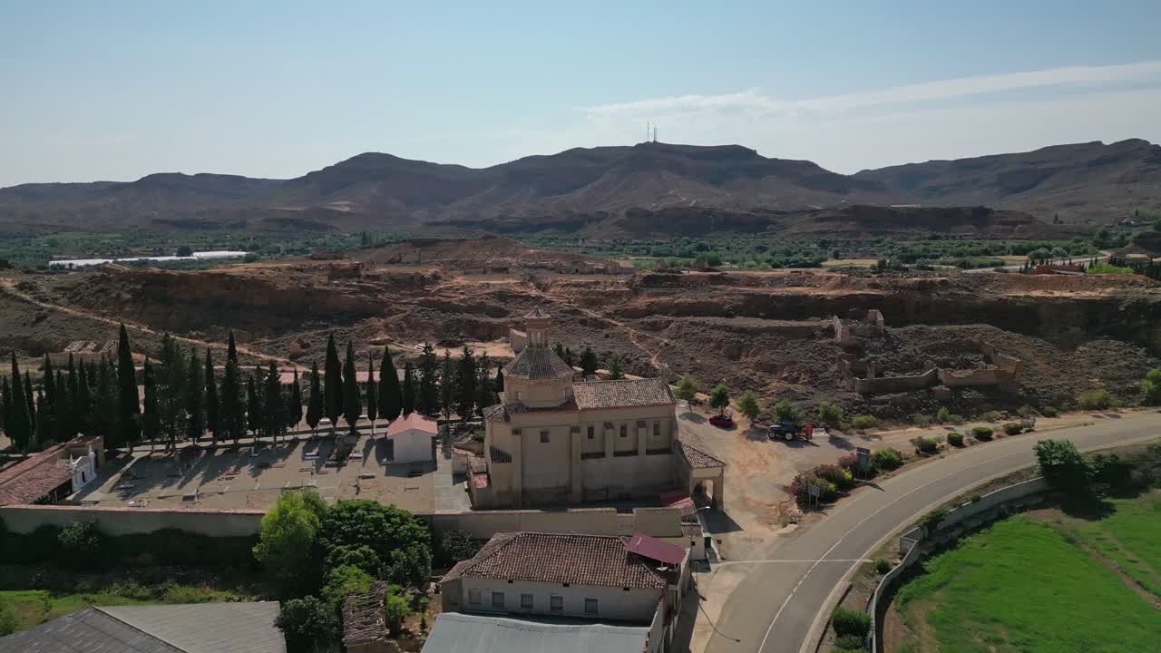 Aerial view of a church and cemetery in a rural village surrounded by arid landscapes and mountains