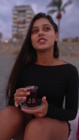 woman enjoying turkish tea by the seaside at sunset