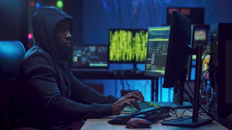 male software developer in a hood sitting at the two computers in the dark and programming some project website