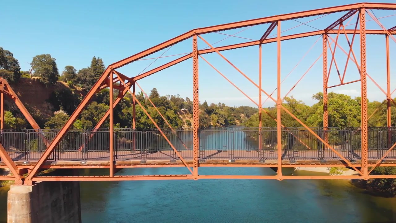 Drone flying sideways over the American River checking out the red Fair Oaks Bridge up close