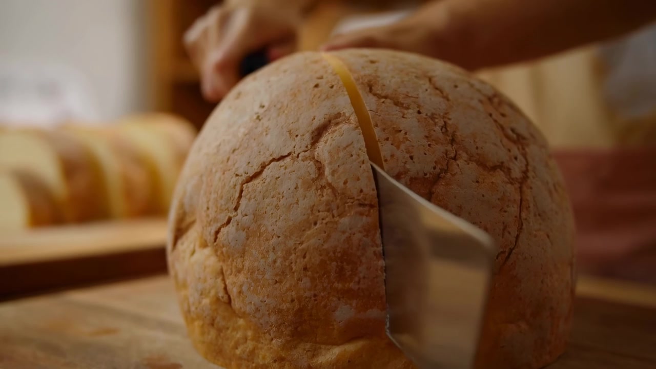 Rustic Round Loaf On Wooden Board, Baker Slicing With Cleaver, Closeup Cracked Golden Crust Revealing Soft