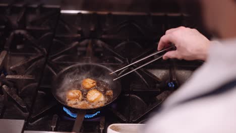 cook turns over the lightly browned fried chicken in a hot pan with oil on the gas stove