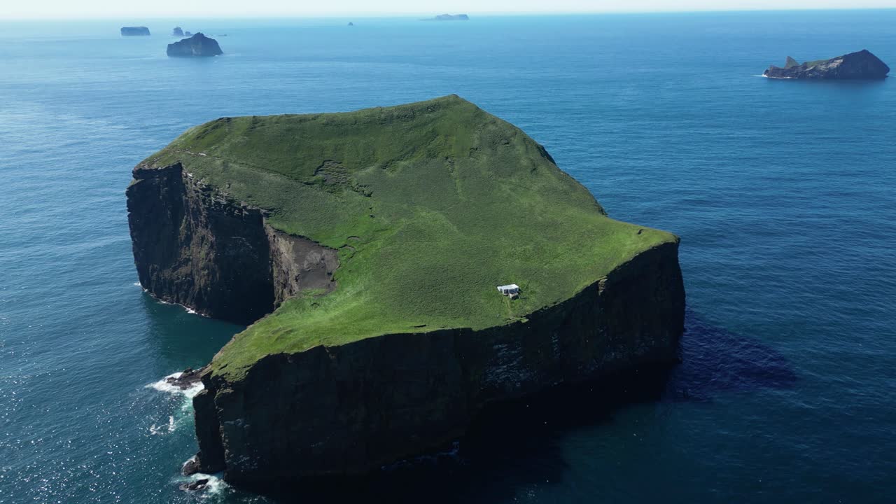 Solitary house on the brim of an island enclosed by shimmering vast blue ocean water. Aerial view