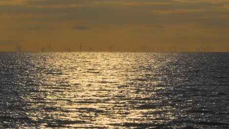 wind turbines on horizon at dusk with sparkling sea