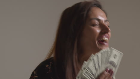 studio shot of excited woman celebrating winning cash prize holding handful of 100 dollar bills