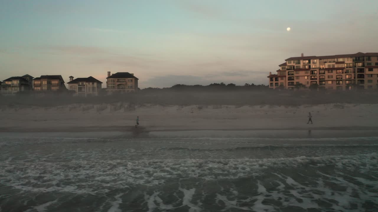 아침에 해안선을 따라 해변에서 달리는 남자, 배경에 럭셔리 빌라 집