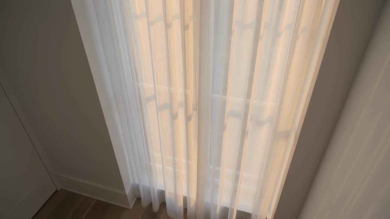Câmera inclinando, revelando cortinas brancas transparentes sobre uma porta alta em casa, mostrando a barra e o chão de madeira