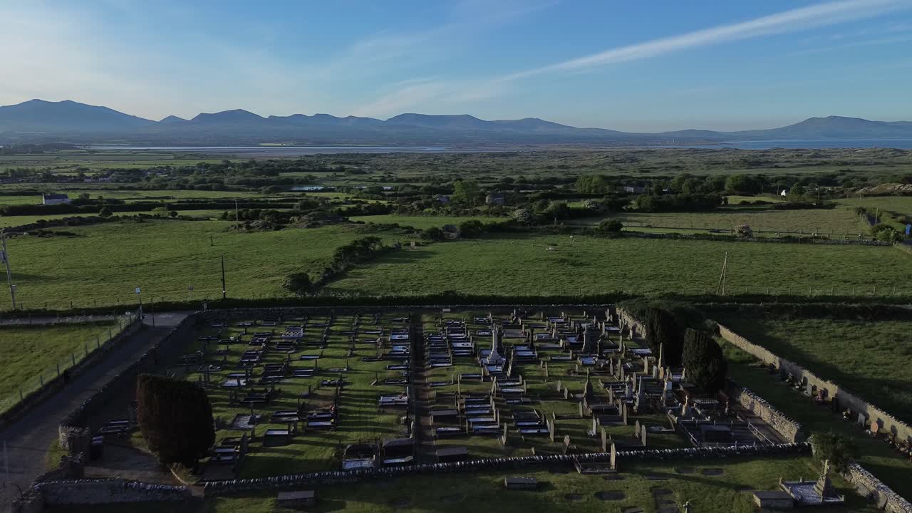 St Peters church in rural Newborough aerial establishing view of Welsh slate gravestones at sunrise