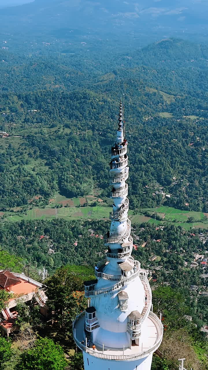 Panning view around the stunning Ambuluwawa Trigonometrical Station with numerous tourists standing on the top. Amazing scenery of Sri Lanka at backdrop. Top view. Vertical video.