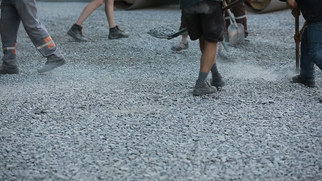 Workers team throw asphalt with shovels at road construction