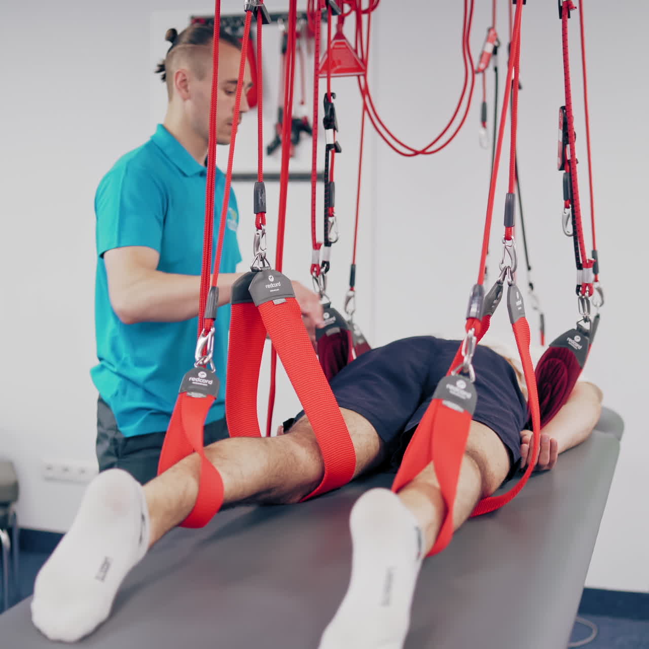 Young therapist is training his client with special ropes in a modern rehabilitation center. Professional trainer works with the patient with a suspension rope system indoors.