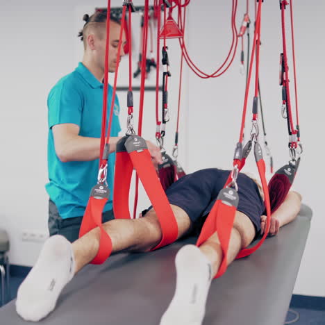 young therapist is training his client with special ropes in a modern rehabilitation center. professional trainer works with the patient with a suspension rope system indoors.