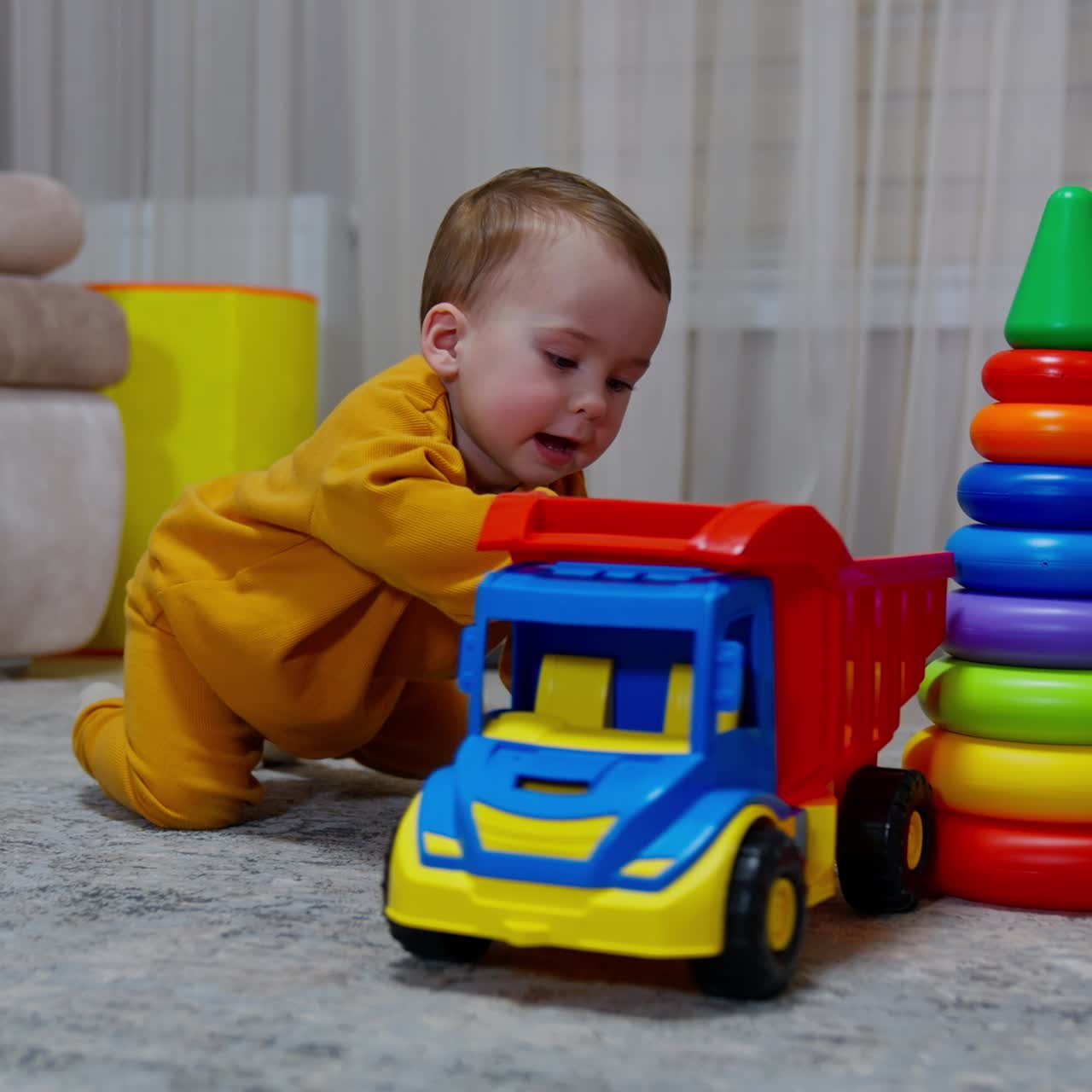Lovely boy crawls up to the toy lorry on the floor. Kid takes the toy and turns it around. Black cat watches the child