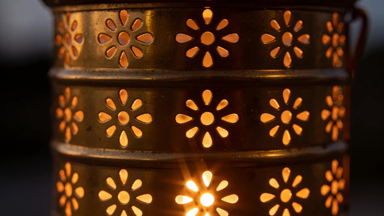 Fiamma tremolante all'interno di una lanterna di metallo che proietta un bagliore floreale sul portico, con manico visibile per la luce del crepuscolo.