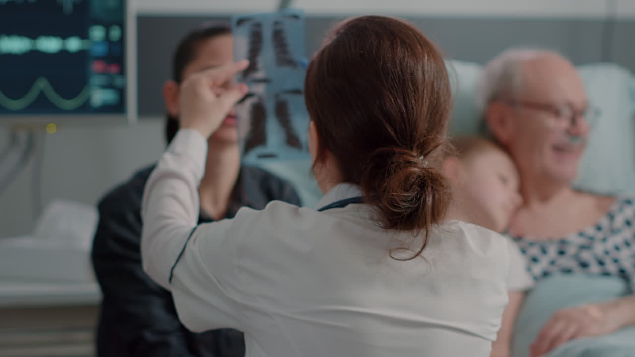 Close up of doctor showing x ray scan to daughter of patient in hospital ward