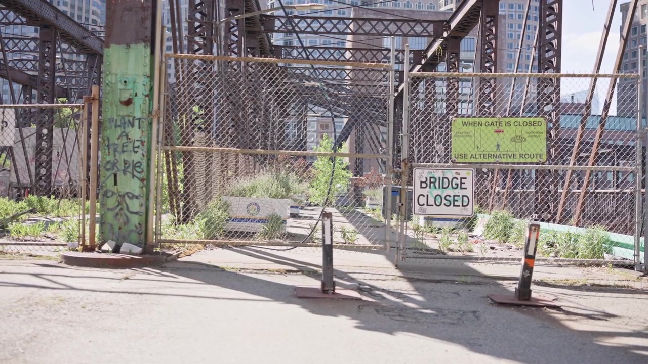 Inquadratura cinematografica di un cartello "Ponte Chiuso" a Boston, Massachusetts, con un ponte storico in acciaio sullo sfondo. L'architettura industriale e l'infrastruttura usurata creano un'atmosfera drammatica.