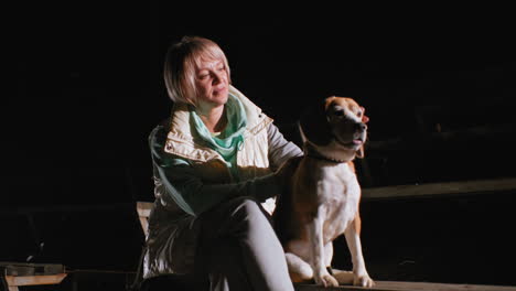 tamer seated at night carefully rubbing puppy removing dirt from its fur under bright light creating tender moment highlighting care, and loving bond between human and dog in dark empty stadium