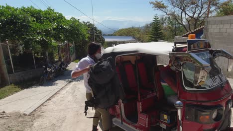 latina woman lifts heavy back pack from tuk-tuk cab on honduras street