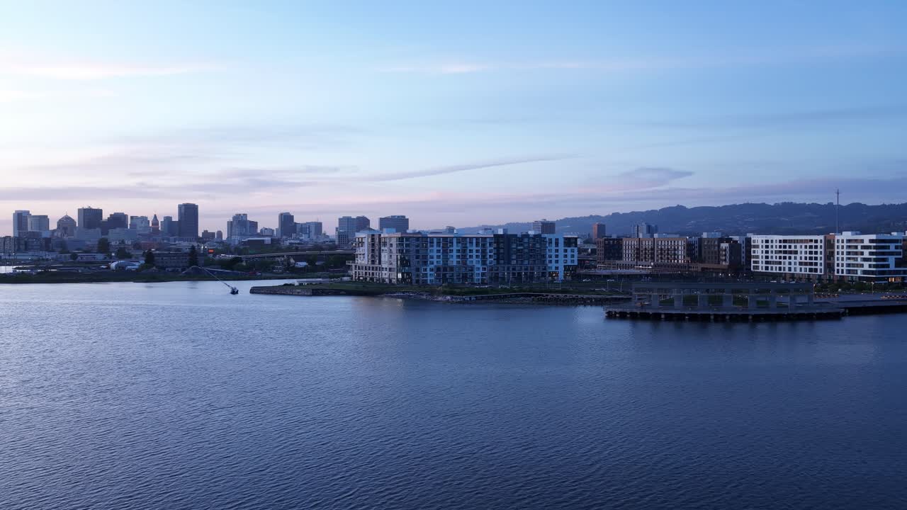 Vista aérea panorâmica sobre as águas calmas do estuário de Oakland em direção à Jack London Square e ao horizonte do centro de Oakland durante um belo pôr do sol na área da baía de São Francisco, Califórnia.