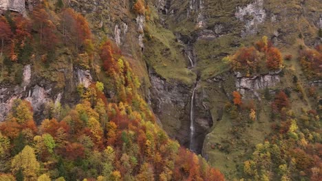 a cascading waterfall plunges down a rocky cliff face, surrounded by a vibrant autumn forest in the klöntal valley, switzerland.