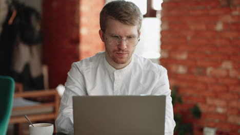 hombre serio en el café está chateando en línea por portátil escribiendo mensajes en el chat en línea y enviando correo electrónico