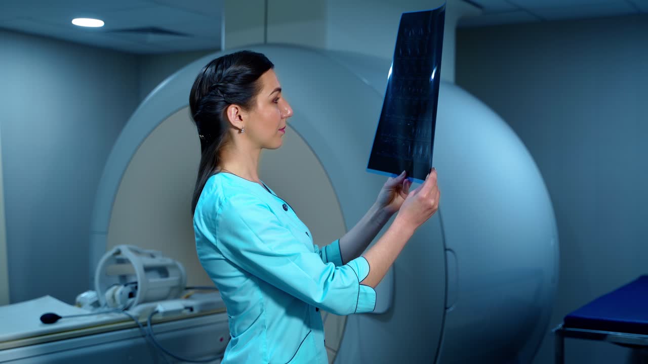 Side view of female specialist with radiography. Specialist holds x-ray photo in arms and carefully researches it. Woman expert dressed in medical coat.