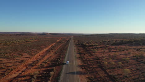 aerial: disparo de dron siguiendo de cerca un vehículo blanco 4wd mientras conduce a lo largo de una carretera de asfalto vacía dentro del interior, al norte de broken hill, australia